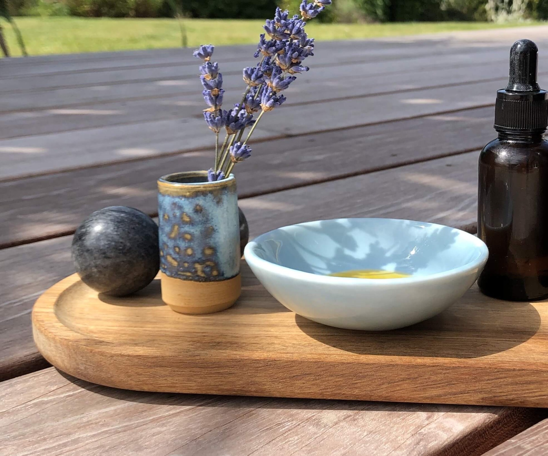 Lavendel i lille krukke, skål med olie og mørk flaske på træbakke ved udendørs terrasse. Nordic Mature Skin Ansigtsolie til Japansk Lifting behandling Klinik W